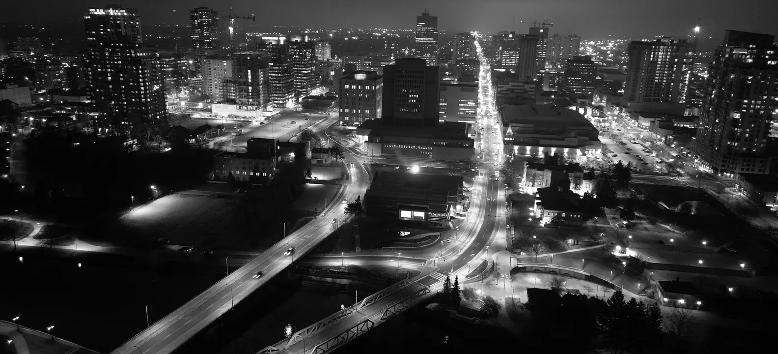 Black and white aerial view of downtown London, Ontario at night, looking up a lit main road between the towers