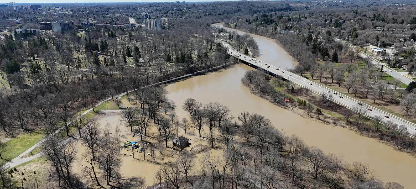 The Thames River in spring flood near Southcrest in London, Ontario, with a road bridge and bare trees along the banks